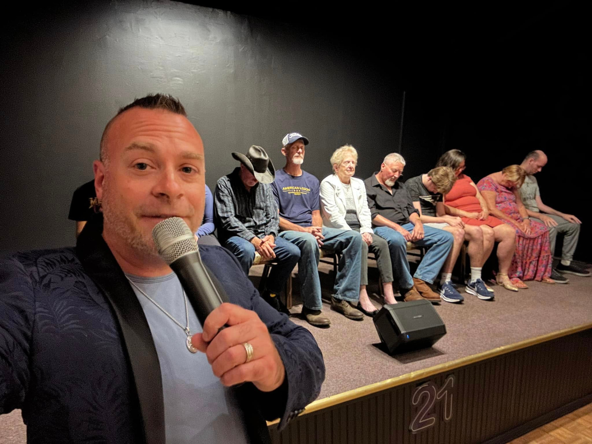 Dan Candell on stage with a row of hypnotized volunteers behind him